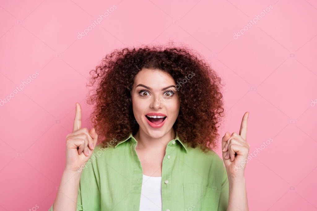 Portrait of ecstatic girl with wavy hairdo wear green shirt indicating at impressive offer empty space isolated on pink color background.