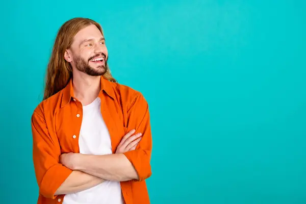 Portrait of positive man with long hairstyle dressed orange shirt arms crossed look at sale empty space isolated on teal color background.