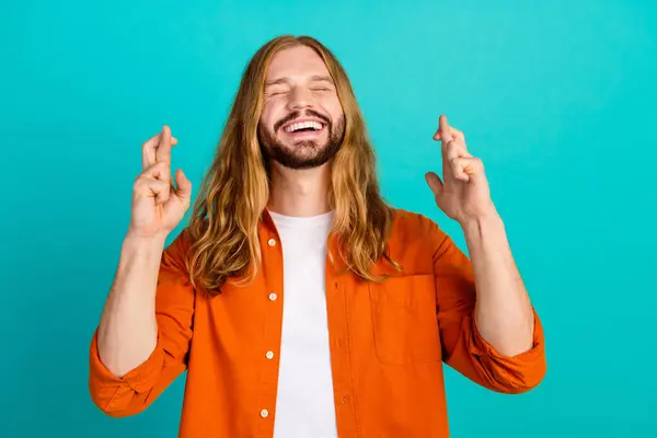 Portrait photo of young jesus christ handsome guy in orange shirt crossed fingers praying miracle isolated on aquamarine color background.