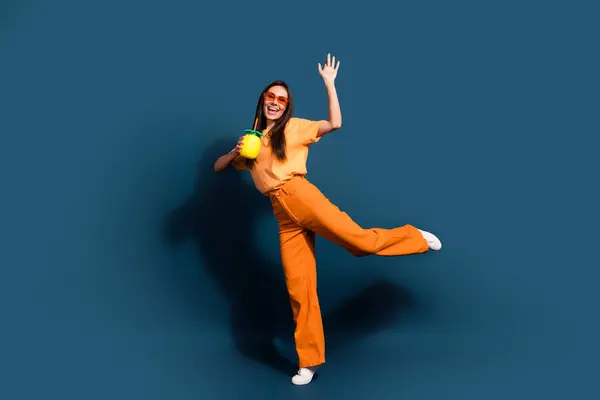 穿着橙色衣服的年轻女士的全身照片夏季迪斯科舞厅喝着奇异的菠萝鸡尾酒 背景是深蓝色的 — 图库照片