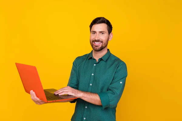 Photo of clever positive cheerful man with stylish haircut dressed dotted shirt hold laptop chatting isolated on yellow color background.