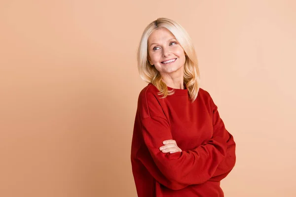 Photo of dreamy excited lady dressed red pullover arms folded looking back empty space isolated beige color background.