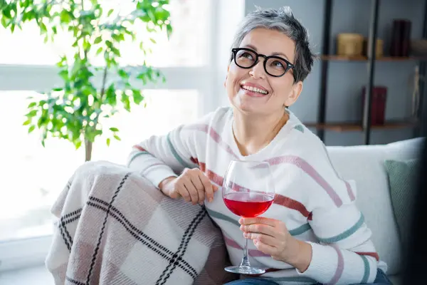 Photo of positive creative minded lady sitting couch hold red wine glass brainstorming imagine chill flat indoors.