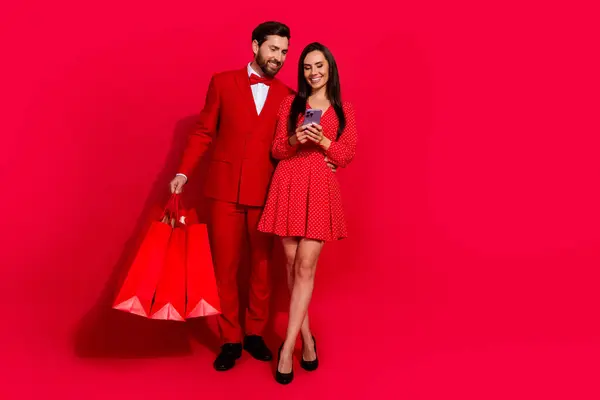 两个优雅情人的全身人像 抱着购物袋 用智能手机空出一个红色背景的空间 — 图库照片