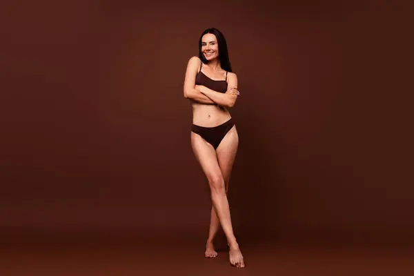 Unfiltered full length photo of lovely tender brunette girl dressed underwear standing arms folded isolated on dark brown color background.