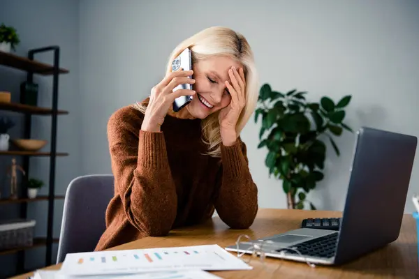 Photo of good mood laughing blonde hair pensioner woman touch forehead laughing during pause phone call in office modern interior indoors.