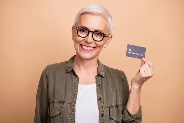 Portrait of middle age woman demonstrate her vip client credit card free drinks lounge in airport isolated on beige color background.