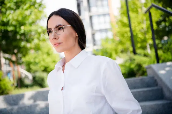 Portrait of stunning lovely serious lady dressed trendy white clothes eyeglasses going office green spark autumn warm day outdoors.