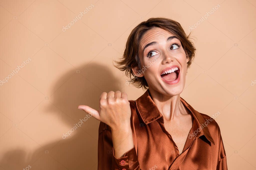 Photo of pretty impressed woman wear silky blouse looking showing thumb empty space isolated beige color background.