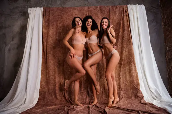 No filters aesthetics studio photo of three cheerful charming sportive girls healthy dieting isolated on beige color textile background.
