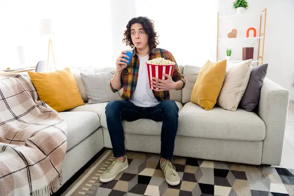 Full length photo of shocked funny guy dressed checkered shirt enjoying can cola pop corn watching intrigue movie indoors house home room.