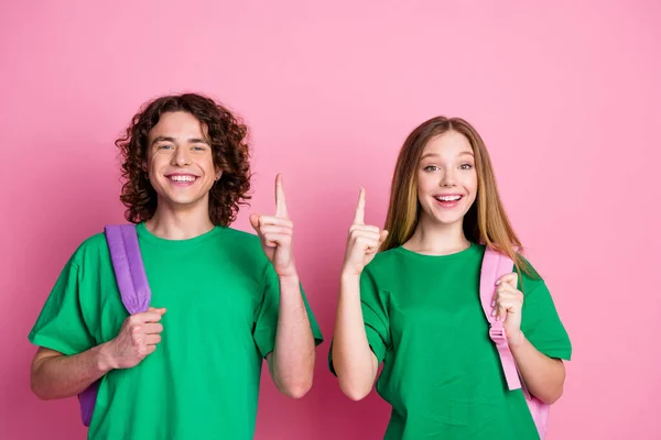ピンク色の背景に隔離された大学で緑色のTシャツのユニフォームとリュックサックを着用した2人の若者の友人の写真 — ストック写真