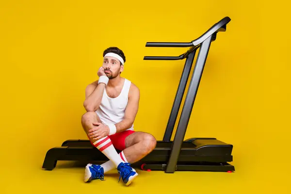 Full body portrait of minded lazy young man sit treadmill look empty space contemplate isolated on yellow color background.