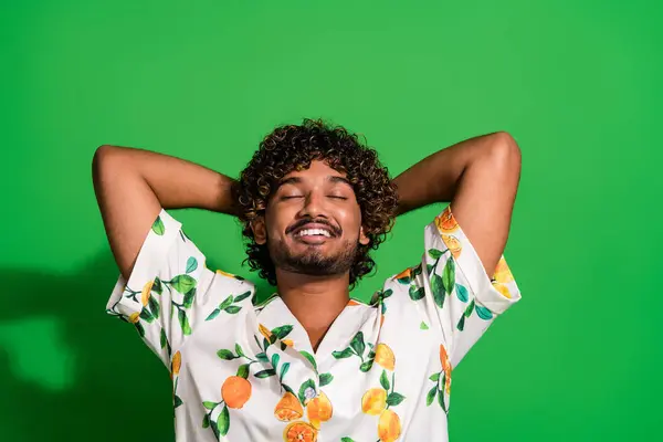Photo of funky dreamy arabian man wear print shirt closed eyes arms behind head isolated green color background.
