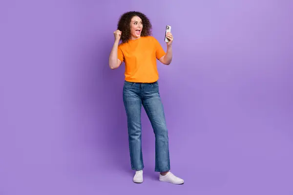 ポジティブなラッキーな女性の完全な長さの写真は オレンジ色のTシャツの勝利ゲーム現代ガジェットは 紫色の背景を隔離しました — ストック写真