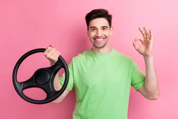 年轻而快乐的男子举着方向盘准备驾驶通过考试的照片 以粉色为背景 — 图库照片
