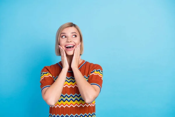 Photo of ecstatic woman with bob hair dressed knit t-shirt staring at offer empty space arms on cheeks isolated on blue color background.