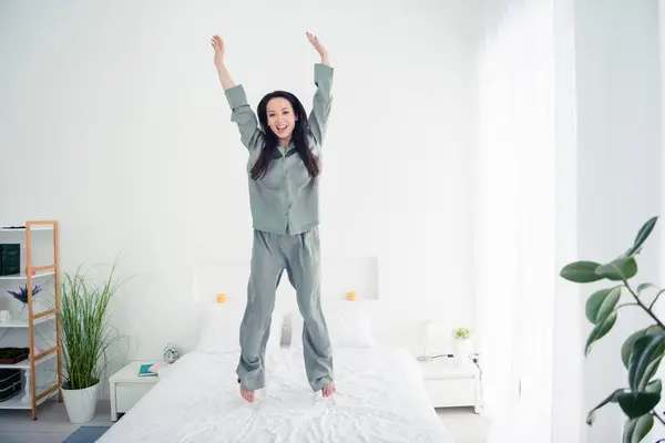 Photo portrait of attractive young woman raise hands jump bed wear trendy gray pajama isolated on white modern interior design.