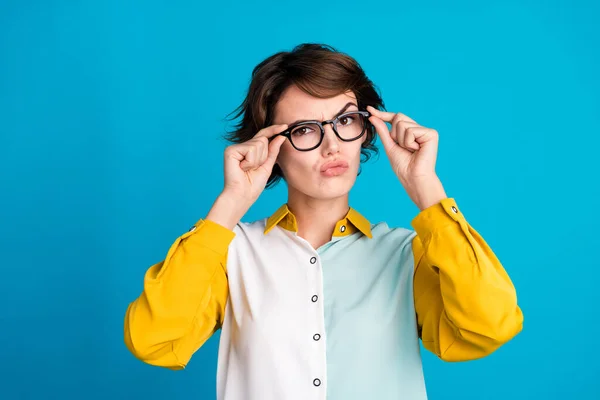 Photo of pensive strict young woman touch eyewear pouted lips with grimace face when looking you isolated on blue color background.
