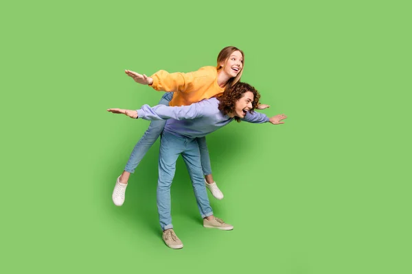 Full body profile portrait of excited cheerful people piggyback arms wings fly empty space isolated on green color background.