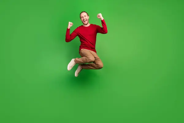 緑色の背景に隔離された宝くじをジャンプする赤い引き出し茶色のパンツを着た楽観的な男のフルサイズの写真 — ストック写真