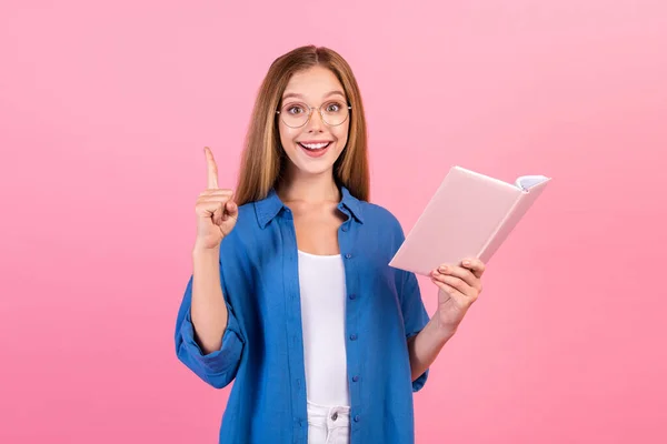 Photo of excited funky lady dressed blue shirt reading story pointing finger up empty space isolated pink color background.