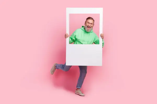 クールな年金受給者の男の実行のフルサイズの写真 ホールドインスタント写真フレームウェア ピンク色の背景に隔離されたトレンディな緑の服 — ストック写真