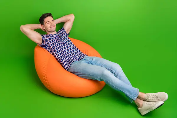 全长的照片 满意的男人穿着时髦的T恤衫 头枕着胳膊睡在豆袋上 绿色背景隔离 — 图库照片