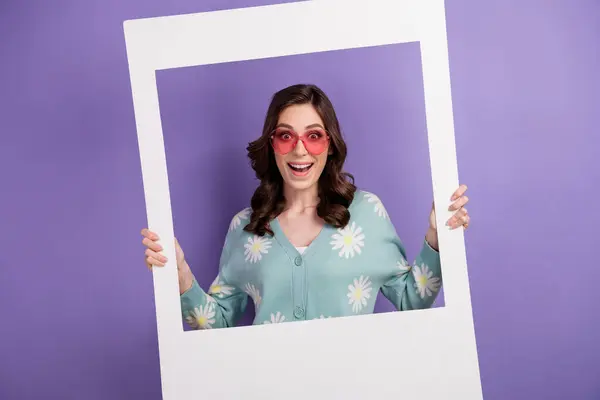 Photo of funky excited lady dressed flower print cardigan pink heart shape eyewear holding photo frame isolated violet color background.