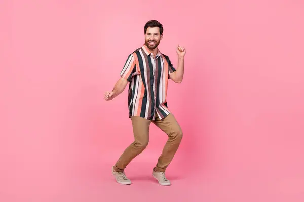 面白いブルネット肯定的な男のダンスのフルサイズの写真は ピンク色の背景に隔離されたストライプシャツブラウンパンツスニーカーを着用します — ストック写真