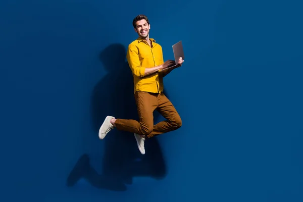 素敵な若い男性ジャンプホールドネットブックマーケターのフル長さの写真は ダークブルーの背景に隔離されたトレンディな黄色の衣服を着用します — ストック写真