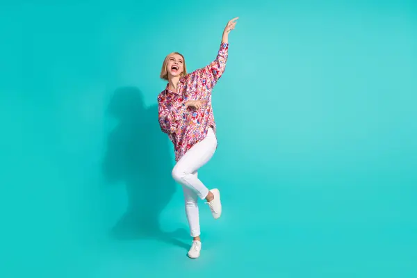 Full size photo of good mood girl wear oversize shirt white trousers dancing look empty space isolated on turquoise color background.