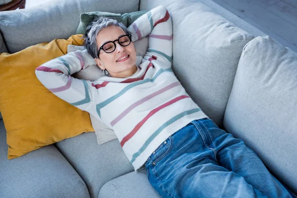 照片上 一位快乐迷人的女士躺在舒适的沙发上 紧闭双眼 在无忧无虑的空余时间里躺在屋里 — 图库照片