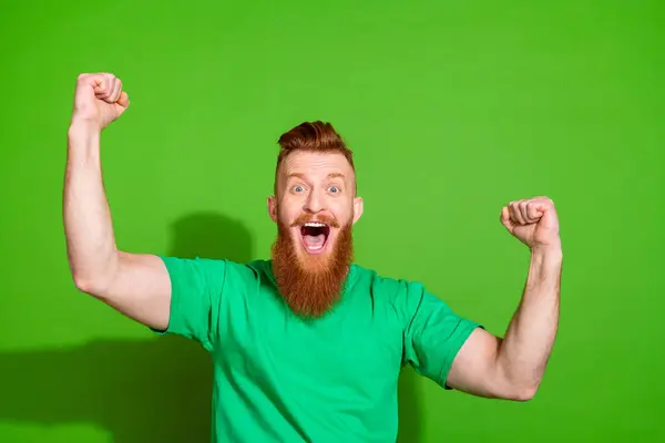 一个喜形于色的疯子 留着长长的红胡子 穿着时髦的T恤 尖叫着 在绿色的背景下孤零零地举起拳头 — 图库照片