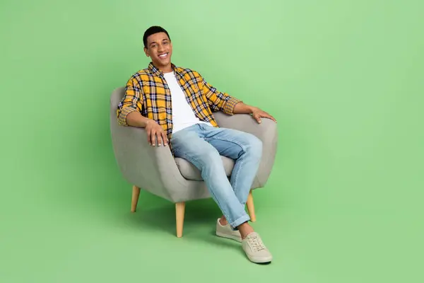 陽気な素敵な男の完全なボディ写真は緑色の背景で隔離された柔らかい椅子の空のスペースを座ります — ストック写真