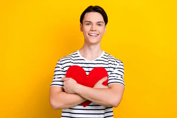 ブルネット髪の満足した男の肖像画 スタイリッシュなTシャツ 黄色の背景に隔離されたバレンタインデーに赤いハートを受け入れる — ストック写真