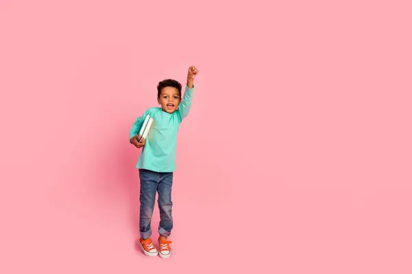 可爱小男孩举起拳头的全长照片超级英雄拿着书穿着时髦的淡蓝色衣服 背景是粉色的 — 图库照片
