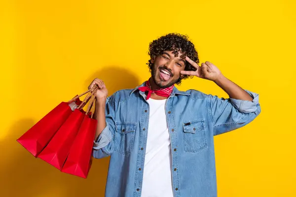 stock image Photo of attractive young man shopping bags show v-sign wink dressed stylish denim clothes red scarf isolated on yellow color background.