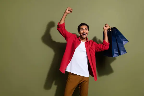 stock image Photo of lucky excited man dressed red shirt rising fist shoppers empty space isolated green color background.