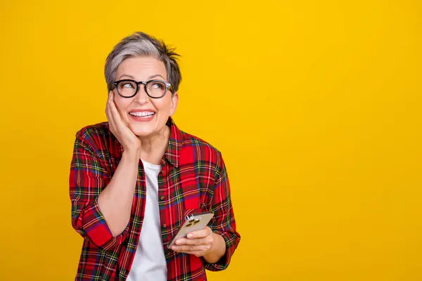 Portrait of creative excited lady toothy smile hold smart phone look empty space isolated on yellow color background.