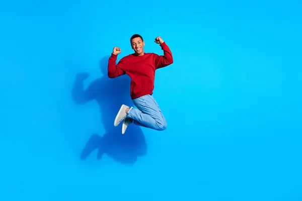 stock image Full size photo of energetic delighted man jump raise fists empty space ad isolated on blue color background.