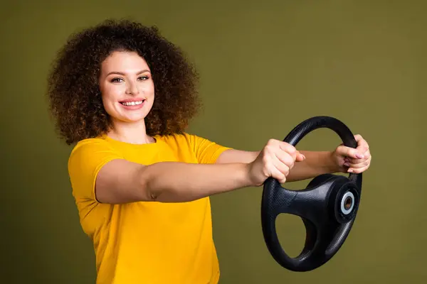 照片上年轻漂亮的卷发女士穿着黄色T恤骑汽车测试驱动模拟器 与卡其色背景隔离 — 图库照片