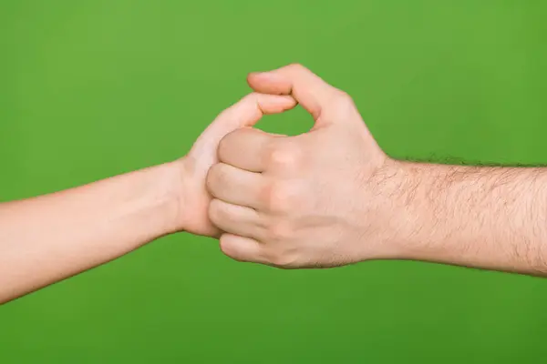 Photo of two people hands palms having fun playing thumb war game isolated green color background.