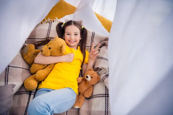 迷人的小女孩躺在地板上的照片 抱着玩具 展示她穿着时髦的黄色衣服 进入幼儿园的游戏室 — 图库照片