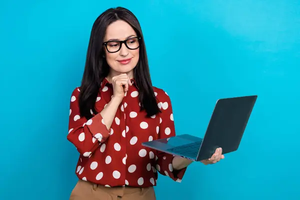 Portrait of clever minded girl with brunette hair wear red shirt in eyewear look at laptop read email isolated on blue color background.
