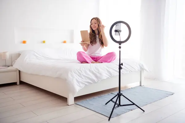 Full size photo of pretty girl sit bed hold mirror apply tone cream record blog smart phone lamp holder bedroom indoors.