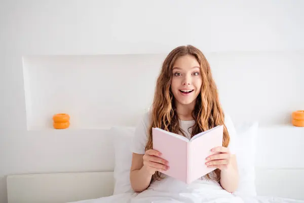 魅力的な驚いた少女の写真は 快適な毛布の下に開かれた本のベッドを保持し 屋内で自由な時間の寝室を過ごします — ストック写真