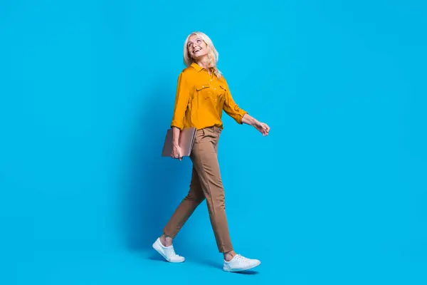 漂亮的退休女性上网本走秀的全长照片 空旷的空间穿着时髦的黄色丝绸衣服 背景是蓝色的 — 图库照片