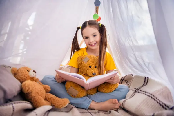迷人的小女孩的肖像坐在地板上抱着玩具看书童话故事穿上时髦的黄色衣服孩子们幼儿园的游戏室 — 图库照片