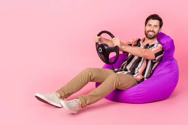 ピンク色の背景に隔離されたビーンバッグに横たわる自動車シミュレーションアプリのテストスキルを運転する幸せな男性の全身の長の写真 — ストック写真